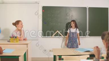 在教室里和老师一起上学。 黑板旁边的女孩展示她的家庭作业